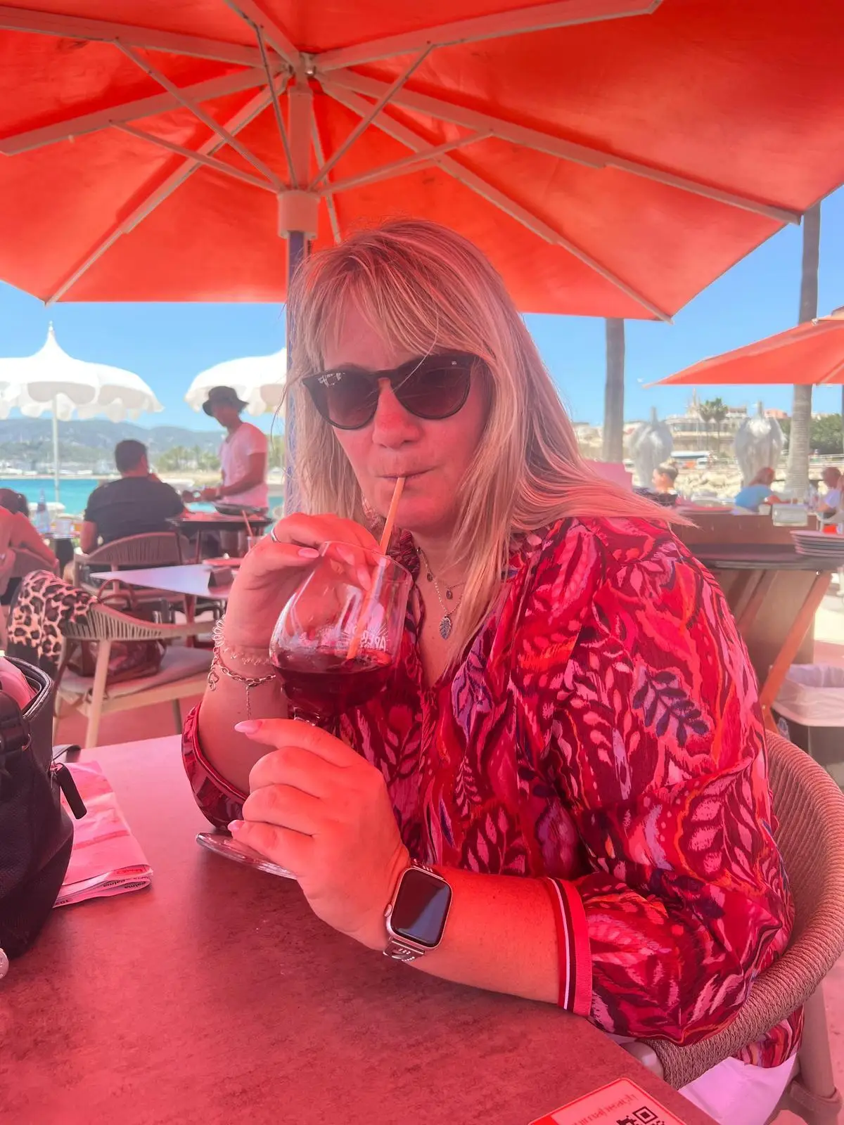 Katrin Caldewei mit einem Aperol Spritz unter einem roten Sonnenschirm sitzend